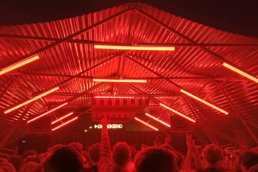 People stand dancing under a Fastival Dome in a Boiler Room setup with red neon lights