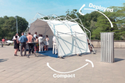 A deployed pop up structure with people and the closed structure for a size comparison next to it.