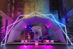 Band on stage under a tent cover in front of tower.