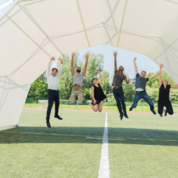 Teammembers jumping under scissor structure tent